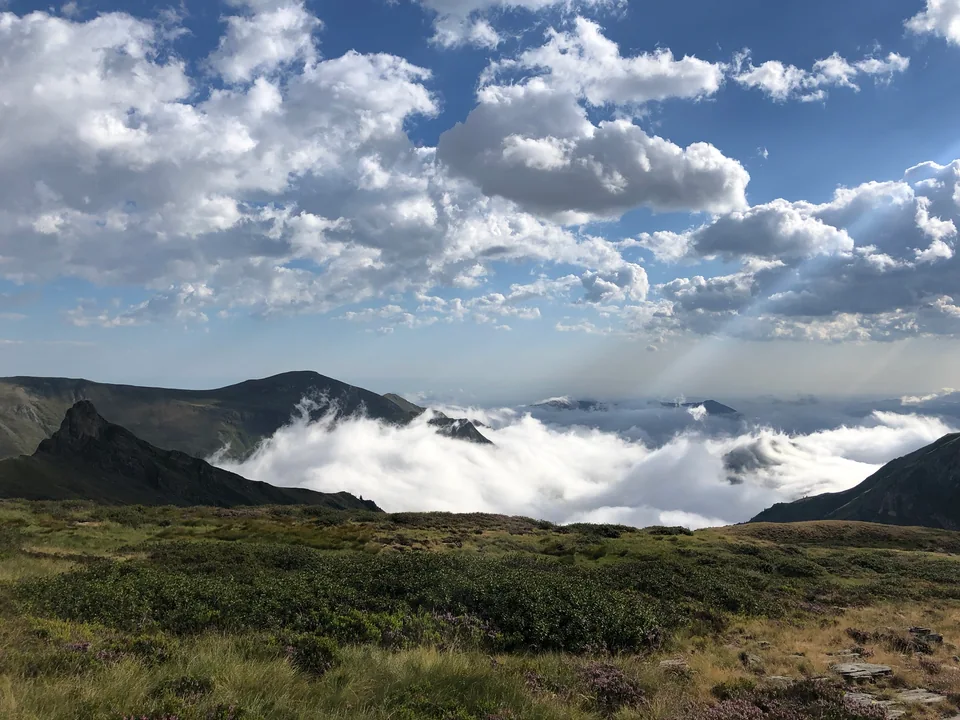 Low clouds fill a mountain valley below grassy ridges and a wide, cloud-filled sky.