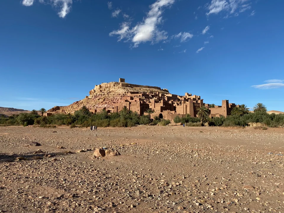 An earthen hillside village, palms, and a stony plain under a clear sky.