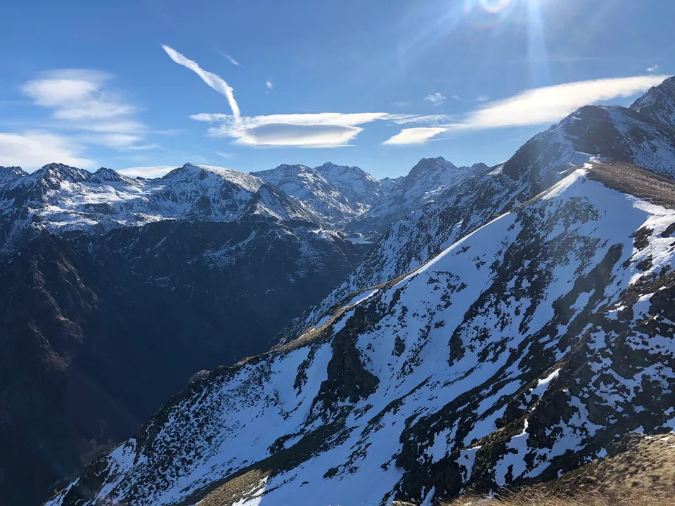 A panorama of snowy mountain ridges and deep valleys beneath wispy clouds.