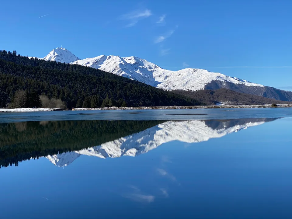 Snowy peaks and dark forest reflected in a blue mountain lake.