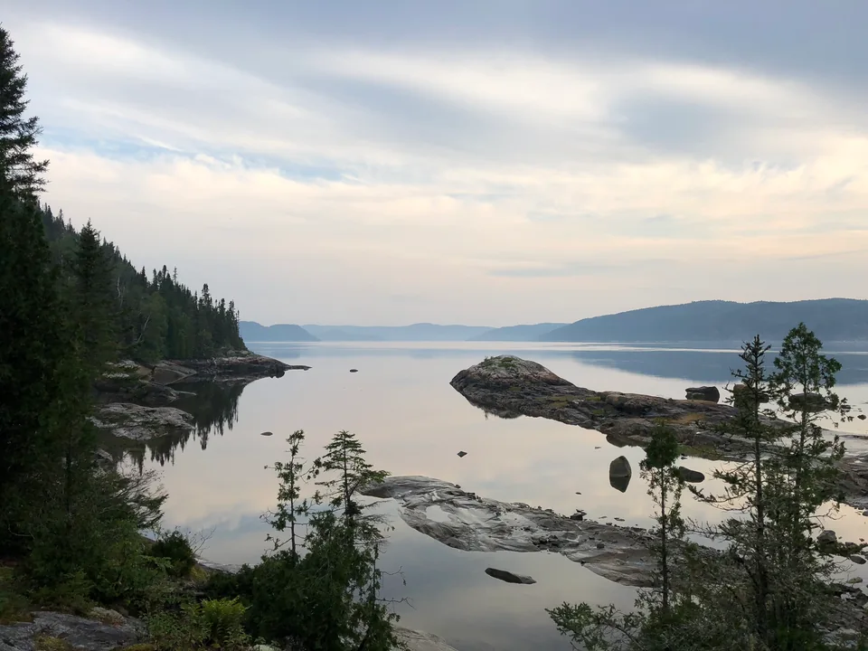 Rocky shores and dark conifers reflected in pale evening water.