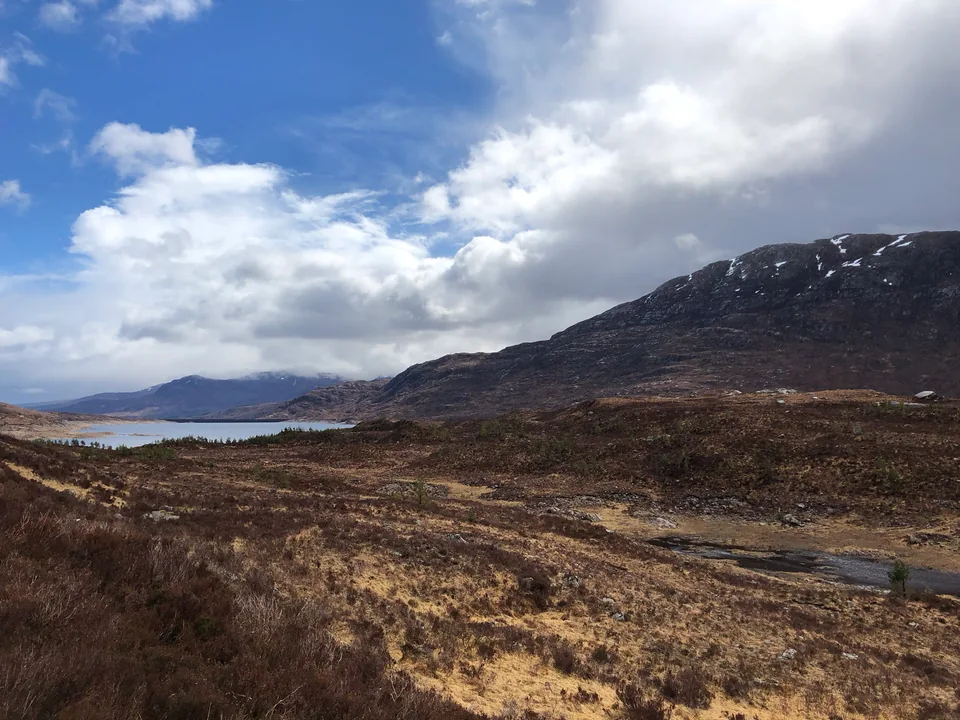An open moor, a distant lake, and dark hills beneath shifting clouds.