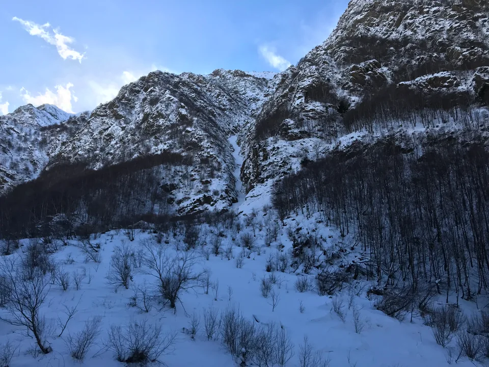 Snow-covered cliffs and bare trees beneath a bright blue sky.
